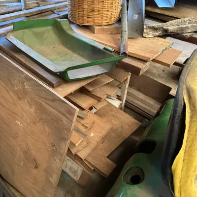 Sale Photo Thumbnail #536: Vintage green John Deere lawn tractor footrests, scrap lumber, and a woven basket in a workshop.