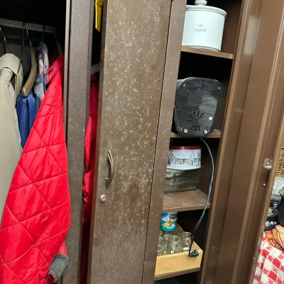 Sale Photo Thumbnail #325: Brown metal storage cabinet storing various household items including outerwear, a Crock-Pot slow cooker, glassware, and small appliances.