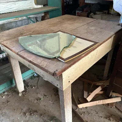 Sale Photo Thumbnail #740: Rustic rustic wooden farm table with straight square legs, featuring a framed certificate and a piece of shaped glass resting on its plank top.