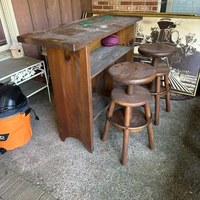 Sale Photo Thumbnail #376: Rustic wooden home bar counter paired with two adjustable screw-top wooden barstools, showing light surface wear.