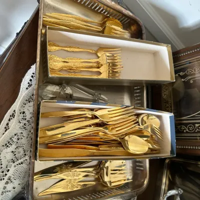 Sale Photo Thumbnail #203: Gold-tone flatware set with ornate floral detailing, organized in boxes atop a silver-plated serving tray with handles.