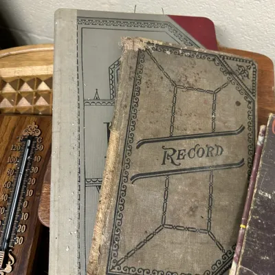 Sale Photo Thumbnail #116: Collection of antique hardcover record books and ledgers alongside a decorative wooden wall thermometer.