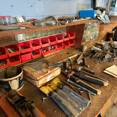 Sale Photo Thumbnail #506: Workshop workbench area featuring red small-parts organizer bins, vintage hand planes, chisels, ratchets, and loose hardware.