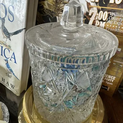 Sale Photo Thumbnail #686: Cut crystal biscuit jar with a matching lid, sitting on a brass-tone metal dish, featuring intricate starburst and pinwheel geometric patterns.