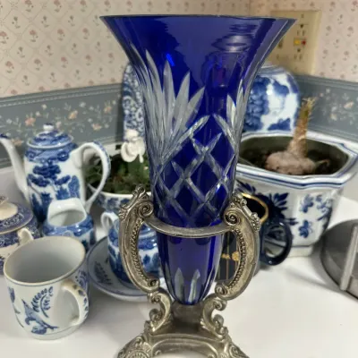 Sale Photo Thumbnail #703: Cobalt blue cut-to-clear crystal trumpet vase resting in an ornate silver-plated or pewter stand.