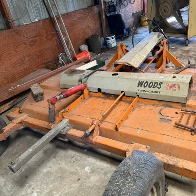 Sale Photo Thumbnail #557: Woods 121 Twin-Cadet pull-type rotary mower attachment showing weathered orange paint, dual wheels, and hydraulic lift cylinders.