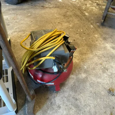 Sale Photo Thumbnail #577: Portable red pancake air compressor with an attached yellow hose, showing signs of light workshop use.