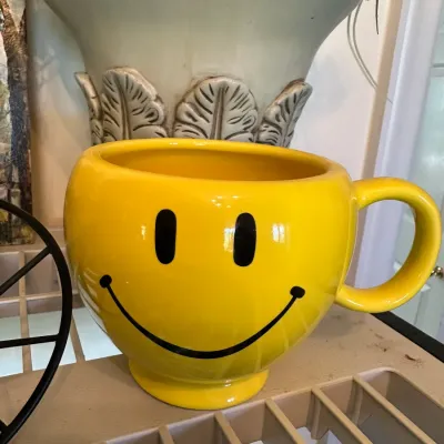 Sale Photo Thumbnail #675: Large yellow ceramic smiley face mug or planter sitting on a shelf.