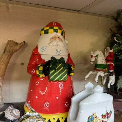 Sale Photo Thumbnail #47: Whimsical glazed ceramic Santa Claus cookie jar holding a present, displayed alongside Christmas table decor and a small carousel horse figurine.