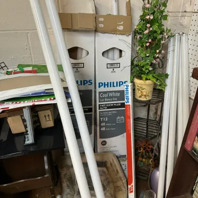 Sale Photo Thumbnail #311: Selection of Philips T12 40-watt fluorescent light bulbs, both loose and in original cardboard packaging, stored alongside household decor items.