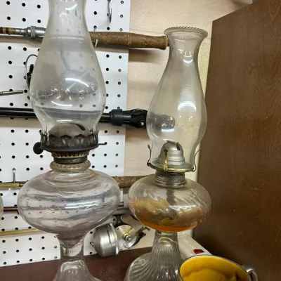 Sale Photo Thumbnail #42: Pair of vintage clear glass oil lamps with metal burners and glass chimneys, featuring molded pedestals and aged hardware.