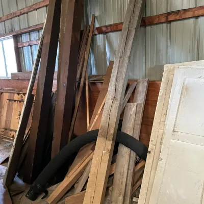 Sale Photo Thumbnail #213: Collection of salvaged wood lumber, rustic beams, and vintage doors leaning against a pole barn wall.