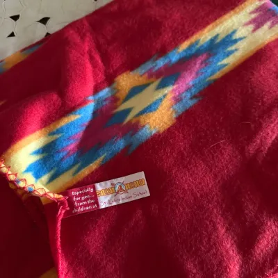 Sale Photo Thumbnail #604: Bright red fleece blanket featuring a Southwest geometric border pattern, complete with an attached St. Labre Indian School tag.