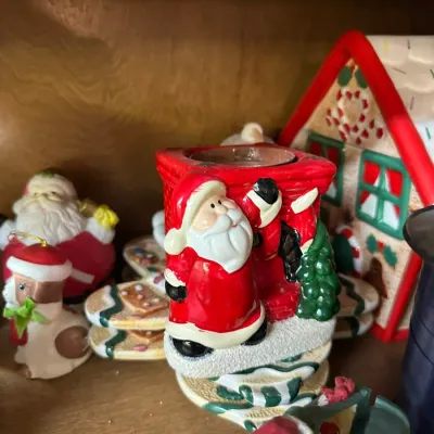 Sale Photo Thumbnail #301: Collection of holiday figurines, featuring a ceramic Santa Claus chimney tea light holder and a gingerbread house.