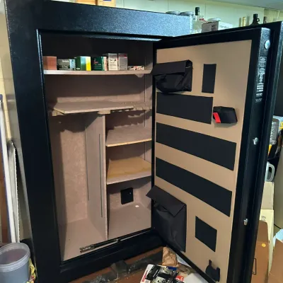 Sale Photo Thumbnail #282: Large black standing gun safe with door storage pouches and adjustable interior shelving containing a few boxes of ammunition.