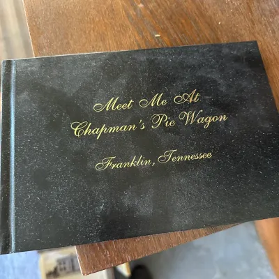 Sale Photo Thumbnail #436: Hardcover book titled "Meet Me At Chapman's Pie Wagon, Franklin, Tennessee" with gold foil script lettering on a black cover.