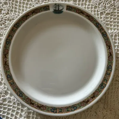 Sale Photo Thumbnail #594: Vintage ceramic rimmed plate or shallow bowl featuring a floral patterned border and a sailing ship motif at the top, resting on a white crochet tablecloth.