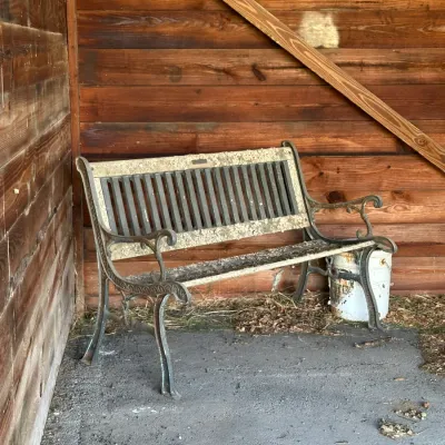 Sale Photo Thumbnail #268: Cast iron and wood garden bench showing heavy weathering and debris, positioned against a rustic wooden wall.
