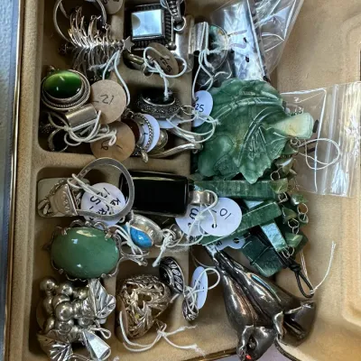 Sale Photo Thumbnail #406: Assorted vintage sterling silver and gemstone jewelry arrayed inside a beige velvet-lined case, featuring jade pieces, rings, brooches, and tagged pendants.