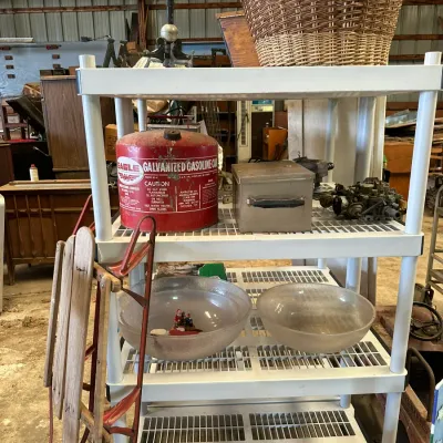 Sale Photo Thumbnail #569: White plastic shelving unit holding various goods including a vintage red Eagle galvanized gas can, glass mixing bowls, and a woven basket, with a vintage wooden sled leaning against the side.