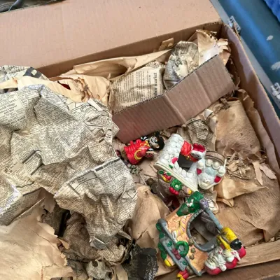 Sale Photo Thumbnail #562: Cardboard box containing vintage hand-painted Christmas figurines and ornaments packed in crumpled newspaper.