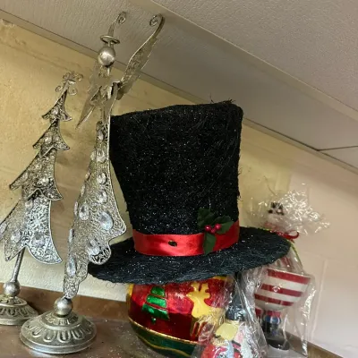 Sale Photo Thumbnail #302: Festive holiday decor assortment, including a black glitter top hat with a red ribbon accent, a hand-painted glass ornament base, and ornate silver-tone metal Christmas tree figurines.