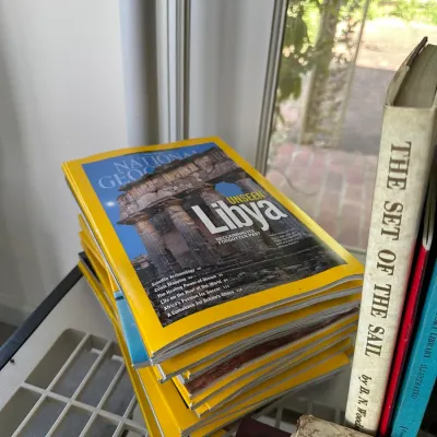 Sale Photo Thumbnail #262: Stack of National Geographic magazines alongside hardback books resting near a window.