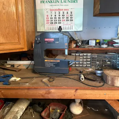 Sale Photo Thumbnail #748: Craftsman 10-inch band saw sitting on a workshop workbench alongside various hand tools and hardware storage cabinets.
