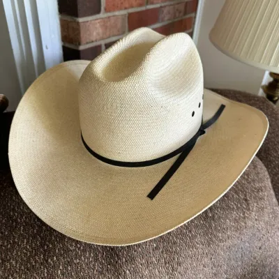 Sale Photo Thumbnail #632: Natural woven straw cowboy hat with a thin black ribbon band and side ventilation eyelets.