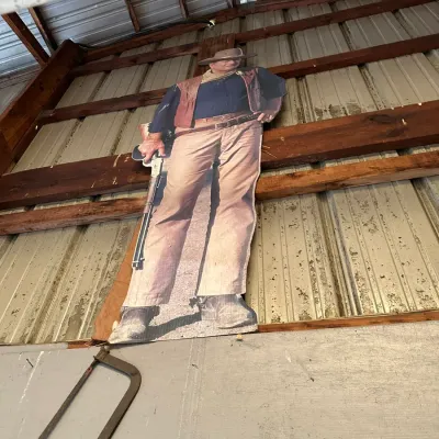 Sale Photo Thumbnail #742: Life-size cardboard standee cutout of John Wayne as a cowboy, mounted inside a barn or shed.