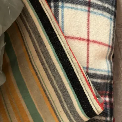 Sale Photo Thumbnail #360: Folded wool blanket featuring a striped border alongside a classic red, black, and blue tartan plaid pattern.