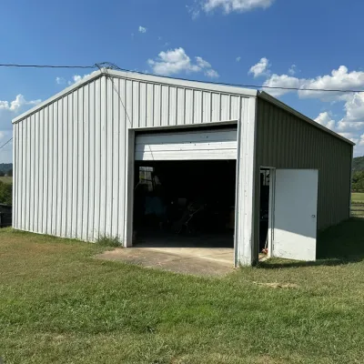 Sale Photo Thumbnail #279: Large metal pole barn or workshop building with roll-up garage door and side pedestrian entrance.