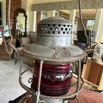 Sale Photo Thumbnail #229: Vintage metal railroad lantern featuring a deep red glass globe, protective wire cage, and wire bail handle.