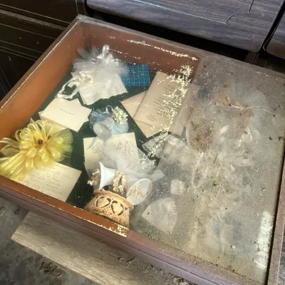 Sale Photo Thumbnail #519: Vintage glass-topped display case containing wedding memorabilia, ribbons, and invitation cards, showing significant dust and age-related wear.