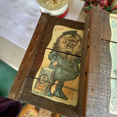 Sale Photo Thumbnail #162: Vintage wooden crate feature with an anthropomorphic Lion Coffee advertising graphic on the slatted panel.
