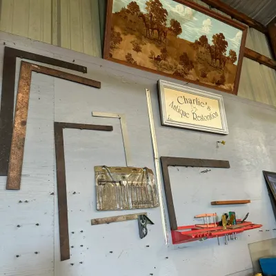 Sale Photo Thumbnail #508: Workshop wall displaying various vintage framing squares, drill bits, and tools, mounted below framed artwork and a custom sign.