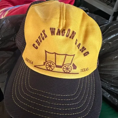 Sale Photo Thumbnail #601: Vintage yellow and brown trucker hat featuring a 'Chuck Wagon Gang Odessa Texas' graphic with a covered wagon.