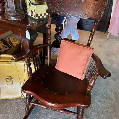 Sale Photo Thumbnail #191: Antique carved wooden rocking chair featuring intricate crest detail, turned spindles, and a dark brown padded leather insert seat.