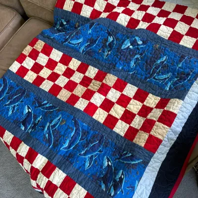 Sale Photo Thumbnail #605: Handcrafted patchwork quilt featuring alternating bands of red-and-cream checkerboard patterns and blue orca whale printed fabric.
