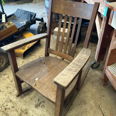 Sale Photo Thumbnail #520: Antique Mission Oak rocking chair featuring wide flat armrests and a slatted backrest, showing wear and dust from storage.