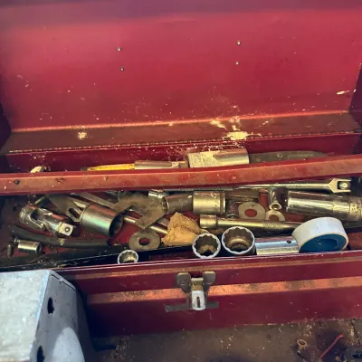 Sale Photo Thumbnail #485: Vintage red metal toolbox filled with various hand tools, socket sets, and hardware pieces, showing typical signs of wear and age.