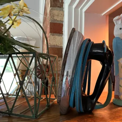 Sale Photo Thumbnail #196: Vintage General Electric clothes iron with a black handle and blue wrapped cord resting on a wooden shelf next to decorative items.