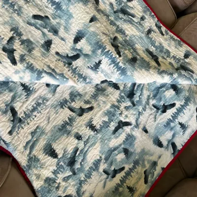 Sale Photo Thumbnail #606: Handmade quilted throw blanket featuring a printed motif of birds in flight over pine trees with a red stitched trim.