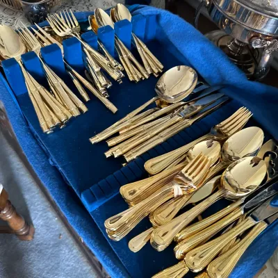 Sale Photo Thumbnail #202: Gold-toned flatware sets presented in a blue velvet-lined storage tray, including faux-bamboo and classic beaded handle styles.