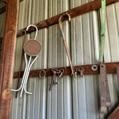 Sale Photo Thumbnail #476: Collection of vintage barn items hanging on a metal wall, including a folding cane seat, a bentwood walking cane with wire attachment, and various metal hardware pieces.