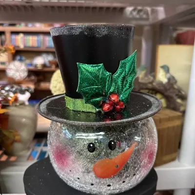 Sale Photo Thumbnail #18: Festive snowman candle holder featuring a cracked glass head and a black top hat adorned with holly leaves and red jingle bells.
