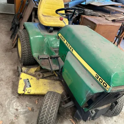 Sale Photo Thumbnail #533: Vintage John Deere 300 riding lawn mower with under-mounted mower deck, showing surface dust and age-consistent wear.