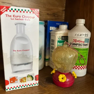 Sale Photo Thumbnail #89: Boxed Euro Chopper kitchen tool displayed alongside garden supplies, household chemical bottles, and a small strawberry-shaped plastic hummingbird feeder.