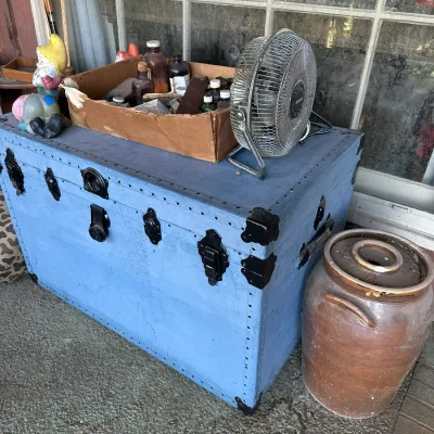 Sale Photo Thumbnail #181: Vintage painted blue steamer trunk with metal hardware, displayed alongside a vintage small electric fan, cardboard box of glass bottles, and a large brown ceramic crock.
