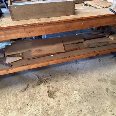 Sale Photo Thumbnail #515: Large wooden workshop bench with lower storage shelf holding various scrap lumber and tools.